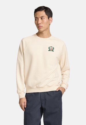 Cremfarbener Pullover mit gerippten Bündchen und Saum, auf der Brust mit einem grünen gestickten Logo und einem Lorbeerdesign. Glatter, weicher Stoff.