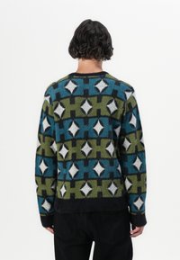 Fargerik mønstrete genser i blått, grønt, svart og hvitt. Har rund hals, lange ermer og en fluffy tekstur med geometriske former.