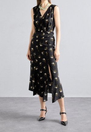 Ärmelloses schwarzes Midikleid mit weißem Blumenmuster, Seitenschlitz, kombiniert mit schwarzen spitzen High Heels und einer auffälligen weißen Halskette.