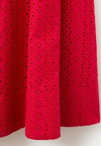 Tissu rouge avec motif floral à œillets brodé créant un design texturé et respirant.