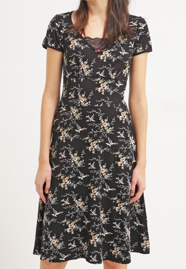 Svart blommig klänning med korta ärmar, spetsdetalj vid halslinningen och en utsvängd kjol. Har ett mönster av fåglar och blommor i ljusa färger.