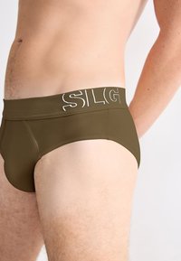 Olivgrüne Unterhosen aus weichem Stoff mit einem elastischen Bund, der den weißen Text "SILG" zeigt. Sie verfügen über ein figurbetontes Design und nahtlose Seiten.