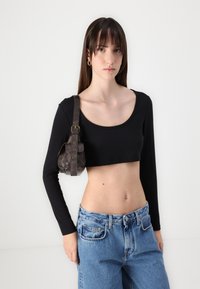 Mustavartinen pitkähihainen crop-top, yhdistettynä korkeavyötäröisiin vaaleansinisiin farkkuihin. Pieni ruskea nahkabag, jossa on hihna, lepää yhdellä olkapäällä.