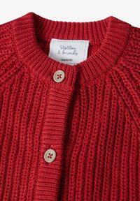 Rode gebreide cardigan met een geribbelde textuur, voorzien van een ronde hals, knoopsluiting en een label met de tekst "Stellou & Friends," maat 62/68.