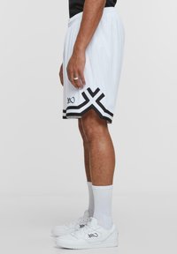 White mesh athletic shorts with a black geometric accent at the hem and a signature detail, paired with white sneakers and socks.