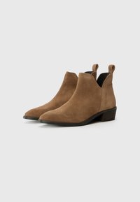 Botas de ante marrón hasta el tobillo con punta afilada, tacón bajo apilado y lengüetas en la parte posterior. Textura lisa con un diseño limpio.