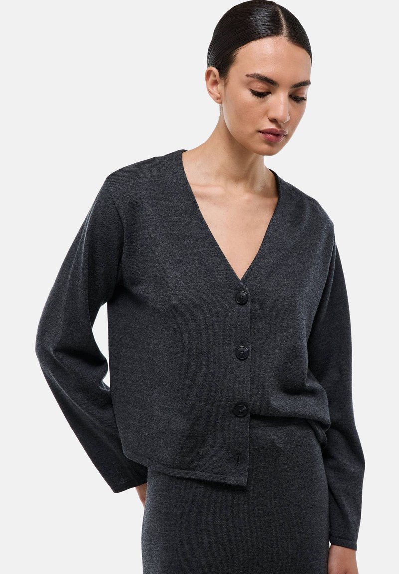 Cardigan gris foncé en maille douce, avec un col en V, des manches longues et cinq boutons noirs sur le devant.