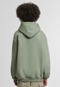 Hooded sweatshirt in muted green, featuring a soft texture, relaxed fit, and ribbed hem. Visible seam details on the back.