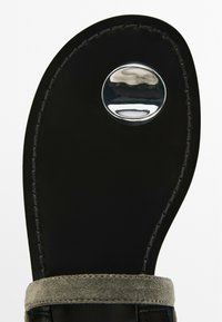 Sandalo nero con soletta in pelle liscia, cinturino in suede grigio e un accento in metallo lucido sulla parte superiore. Design del tacco arrotondato.