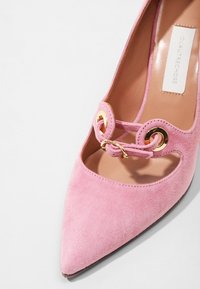 Chaussure à talon haut en suede rose avec un bout pointu et un design découpé. Comprend un détail en boucle en métal doré sur le devant.