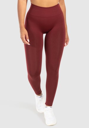 Bordeaux hoge taille legging gemaakt van een gladde, rekbare stof, met een aansluitende pasvorm en zonder zichtbare naden, gecombineerd met witte sneakers.