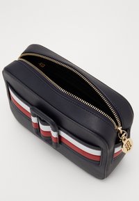 Marineblauwe leren cosmetica tas met gouden rits. Heeft een horizontaal gestreept ontwerp in rood, wit en marineblauw. Inclusief een rechthoekige sluitingselement.