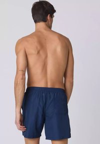 Pantaloni da nuoto blu con vita elasticizzata, due tasche posteriori e un tessuto leggero, mostrati da dietro, senza ulteriori dettagli.