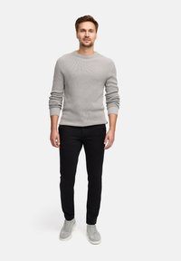 Pull en maille côtelée gris clair avec col rond, pantalon noir ajusté et baskets en daim gris. Modèle se tenant devant un fond uni.