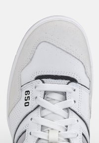 White sneaker with a smooth leather and suede upper, black accents, perforated toe box, and flat white laces. Features model number 650.