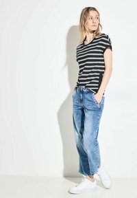Černé a šedé pruhované tričko s krátkým rukávem, spárované se světle modrými širokými džíny a bílými teniskami. Jednoduchý design, casual střih.
