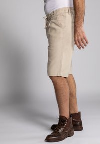 Beige šortky s elastickým páskem, šňůrkou, bočními kapsami a volným střihem, kombinované s hnědými koženými šněrovacími botami.