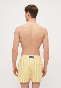 Gelb-weiß gestreifte Badeshorts aus leichtem Material, mit einer Gesäßtasche und einem Markenetikett am Bund.