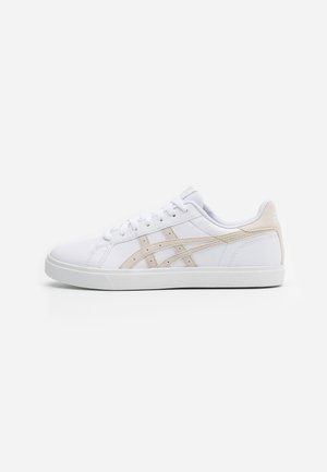Baskets basses blanches avec des bandes latérales beige, des lacets blancs et un col rembourré, montrées en profil gauche sur un fond uni.