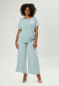 Top azzurro chiaro, fluido, con maniche corte abbinato a pantaloni a gamba larga. Tessuto liscio e vestibilità rilassata, creando una silhouette elegante.