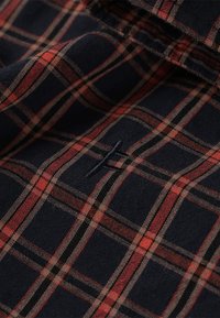 Checkered fabric featuring a dark navy background with red and brown plaid pattern. Includes a small navy logo stitched prominently.
