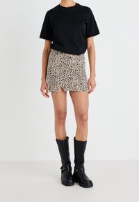 Černé tričko s krátkým rukávem spárované s béžovou minisukní s leopardím potiskem a bočním rozparkem. Nosit s vysokými černými botami po kolena.