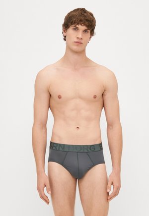 Γκρί ανδρικά σλιπ με ζώνη λογότυπου σε πράσινο χρώμα. Το ύφασμα φαίνεται λείο, εφαρμοστό και έχει ραμμένες λεπτομέρειες στο μπροστινό μέρος.