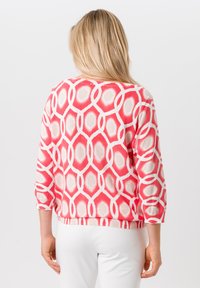 Gebreide trui met een gedurfd roze en witte geometrische print, driekwartmouwen en een ontspannen pasvorm. Zachte textuur met geribde zoom.