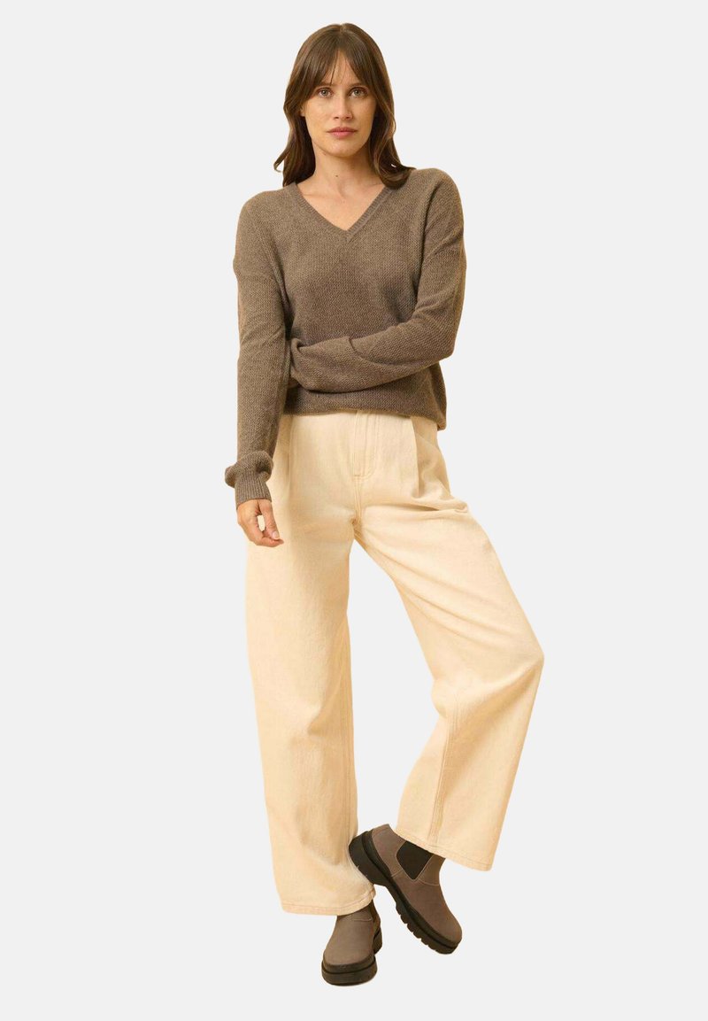 Brązowy sweter z dekoltem w serek, kremowe spodnie typu wide-leg, szare botki za kostkę. Miękka faktura, luźny krój i casualowy design. Prosta, neutralna paleta kolorów.