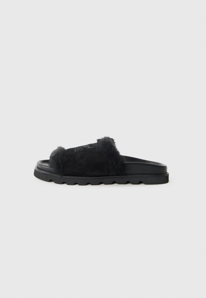 Black slide sandals featuring a soft fur upper, suede straps, and a textured rubber sole with chunky tread pattern.
