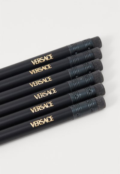 Creioane negre cu branding auriu "Versace", având o radieră la un capăt și un grip texturat. Șase creioane aliniate orizontal.