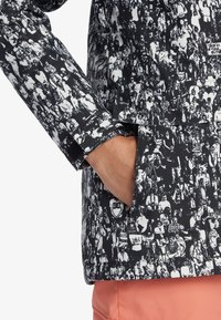 Black and white jacket featuring a densely patterned graphic design, with a flap pocket and smooth texture. Accented by a small brand label.