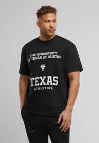Sort bomulds T-shirt med hvid tekst: "THE UNIVERSITY OF TEXAS AT AUSTIN" og "TEXAS ATHLETICS", med en afslappet pasform og korte ærmer.