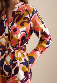 Langärmliges Kleid mit einem bunten Blumenmuster in Pink, Lila und Gelb, mit einem gebundenen Bund und einem tiefen V-Ausschnitt.