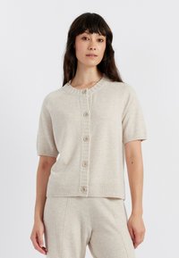 Cardigan lavorato a maglia di un beige chiaro con maniche corte, scollo rotondo e sette bottoni davanti. Presenta polsini e bordo a coste.