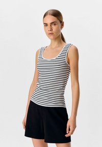 Top sin mangas a rayas blancas y negras con escote redondo y un diseño ajustado, combinado con pantalones cortos negros que muestran una textura acanalada.