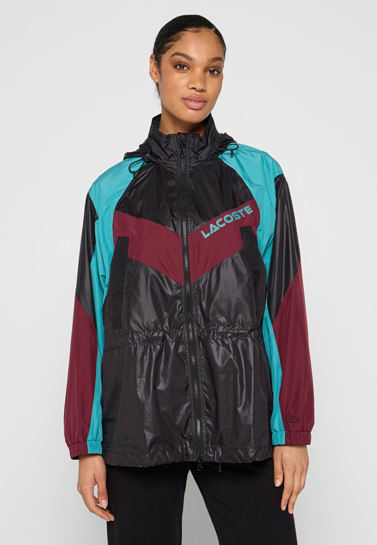 Kurtka przeciwwiatrowa Lacoste, z czarnymi, turkusowymi i bordowymi panelami, zamek błyskawiczny, kaptur na sznurku i elastyczne mankiety. Lekki, błyszczący materiał.