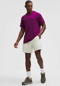 Kortærmet lilla sports t-shirt kombineret med cremefarvede shorts. Grå sneakers og hvide sokker fuldender outfittet, som udstråler en afslappet pasform.