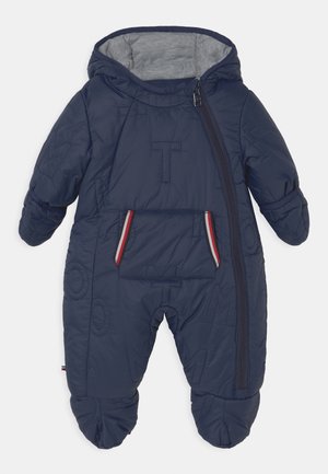 Combinaison de neige matelassée bleu marine pour bébé avec capuche, fermeture éclair diagonale à l'avant, lettres matelassées et une poche avant avec un liseré rouge et blanc.