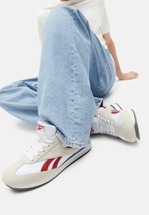 Biele a béžové tenisky s červenými a modrými akcentmi, vyrobené z kombinácie kože a semišu a s textúrovanou gumovou podrážkou.