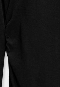 Chemise noire à manches longues en tissu côtelé, vue de côté avec un léger froncement près de la zone sous les aisselles.