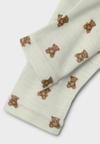 Tissu blanc avec de petits motifs répétitifs d'ours en peluche marron, montrant des bords repliés et des coutures visibles.
