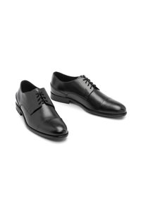 Czarne skórzane pantofle o gładkiej fakturze, z wiązaniem, zaokrąglonym noskiem i subtelnym akcentem na czubku. Niski, odkryty obcas.