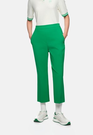 Person wearing bright green cropped pants, white sneakers with green details, white socks, and a white ribbed shirt with green trim.