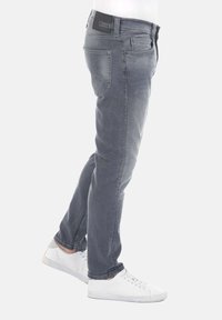 Jeans de mezclilla gris con corte recto, que presentan una etiqueta negra en la cintura, bolsillos traseros, y se combinan con zapatillas blancas.