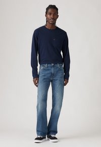 Camisa de manga larga de color azul marino con bolsillo en el pecho, vaqueros rectos descoloridos de color azul y zapatillas negras con suelas blancas. Atuendo casual sencillo.