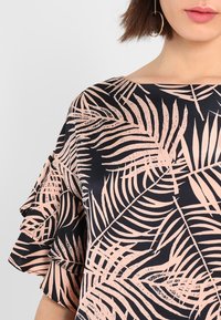 Tmavá blůza s vzorem listů v broskvových tónem, s volánovými rukávy a širokým lodním výstřihem, vyrobená z hladkého materiálu.