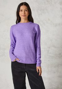 Lila Strickpullover mit langen Ärmeln, rundem Ausschnitt und gerippten Bündchen. Kombiniert mit schwarzen Cordhosen. Texturiertes und lässiges Design.