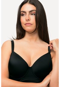 Soutien-gorge rembourré noir avec bretelles réglables, texture lisse et décolleté plongeant ; il dispose d'un renfort à l'intérieur pour le soutien et de coutures discrètes.