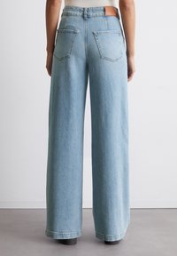 Ljust blå vida jeans med hög midja, med två bakfickor och en läderpatch vid midjan. Mjuk jeanstextur.